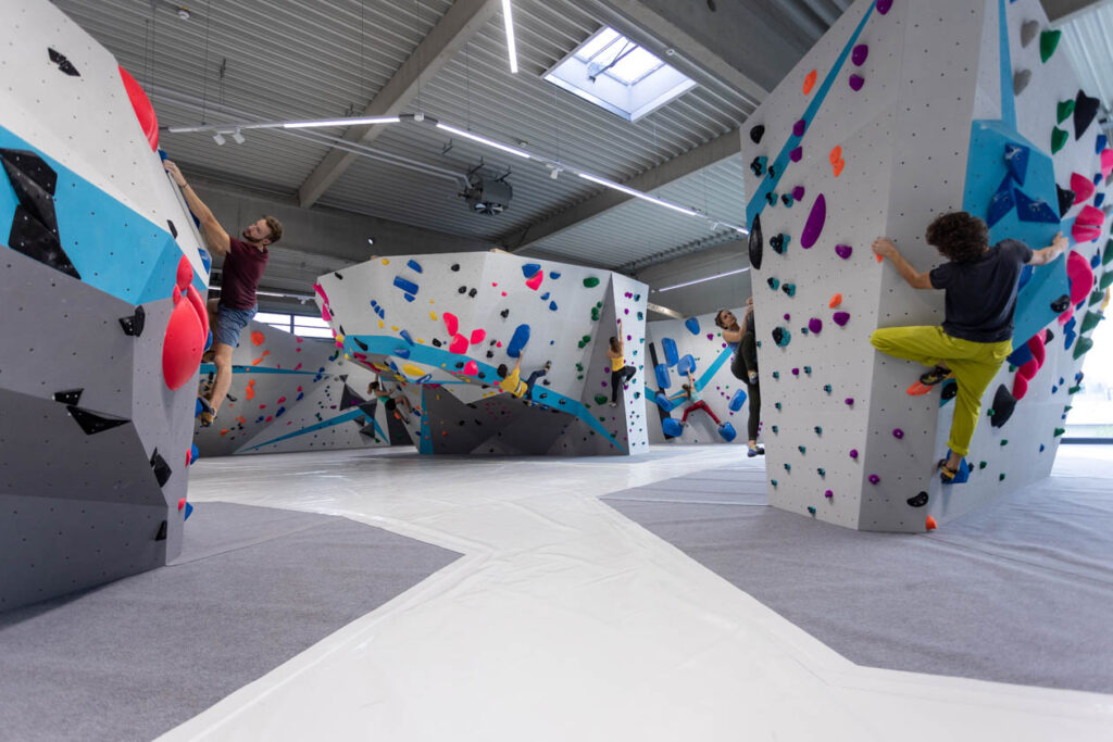 Mehrere Kletterwände in einer Indoor-Boulderhalle mit drei Kletterern.