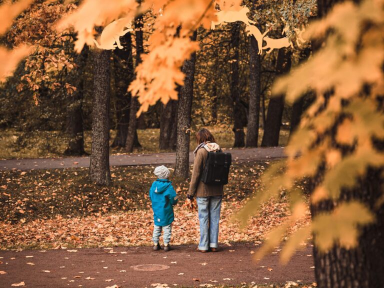 Eine Junge Frau und ein Kind halten sich bei der Hand in einem herbstlichen Wald.