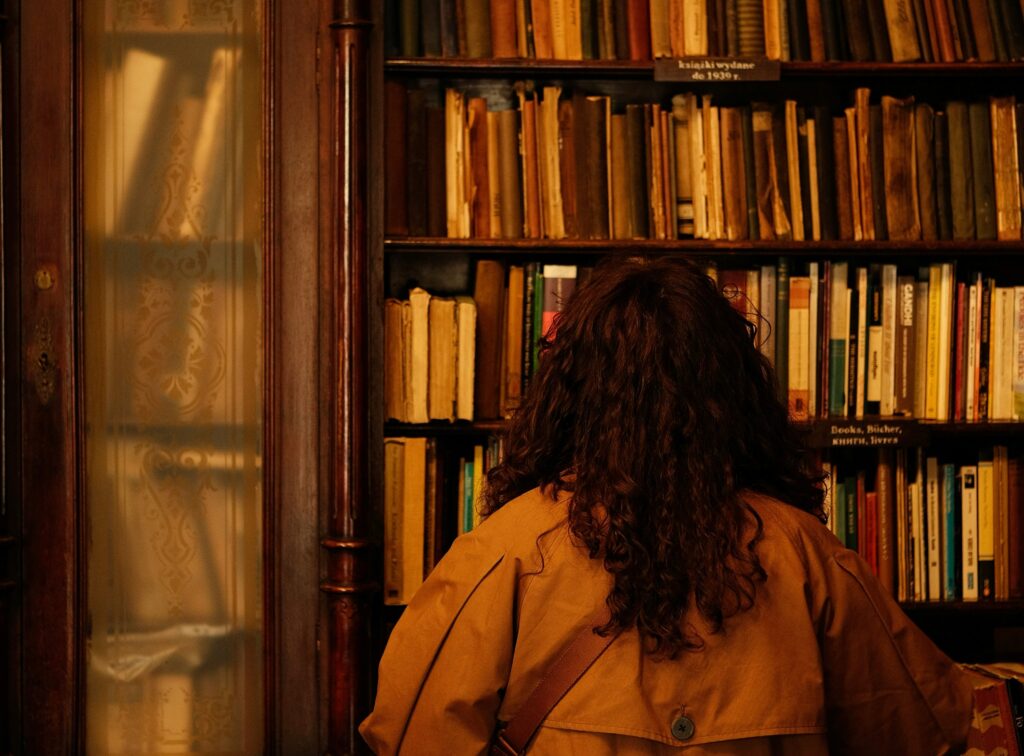 Eine Frau steht vor einem hohen, antiken Bücherregal.