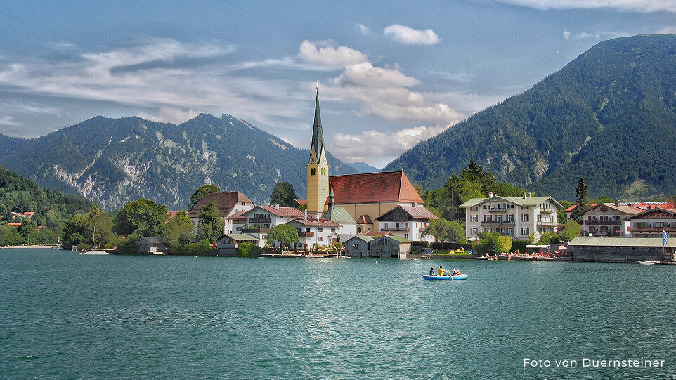 Bild von Tegernsee. Ein Bild von einer Kirche am See mit Bergen im Hintergrund