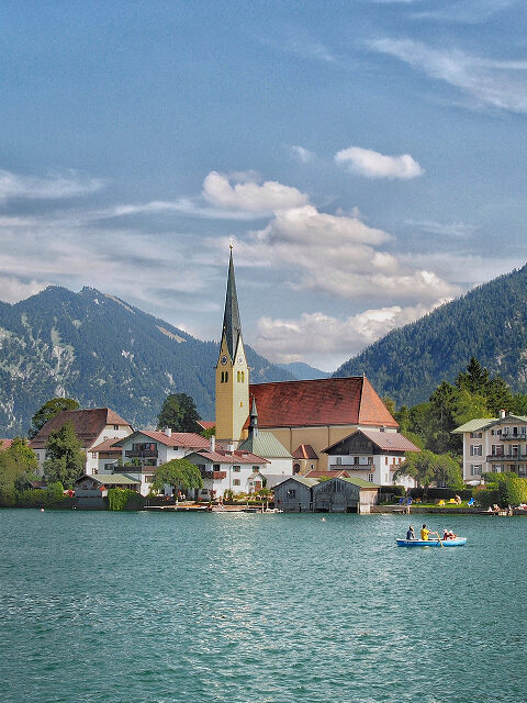 Bild von Tegernsee. Ein Bild von einer Kirche am See mit Bergen im Hintergrund