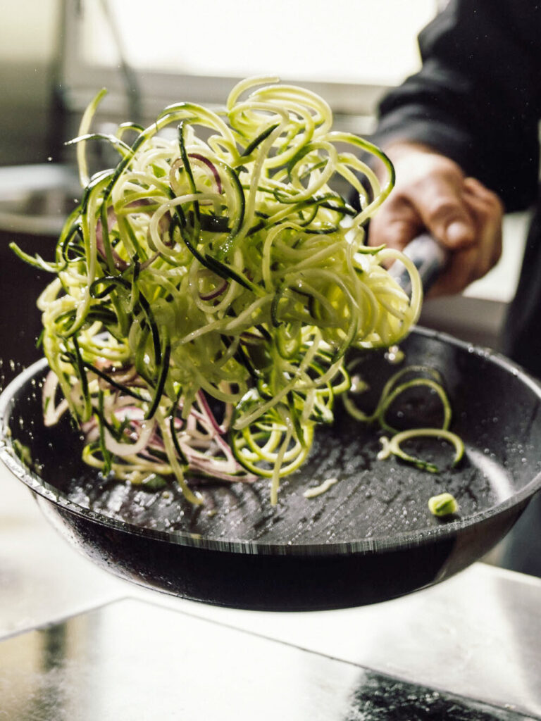 Aufnahme von Koch wie er Zucchini-Nuddeln in der Pfanne schwenkt.