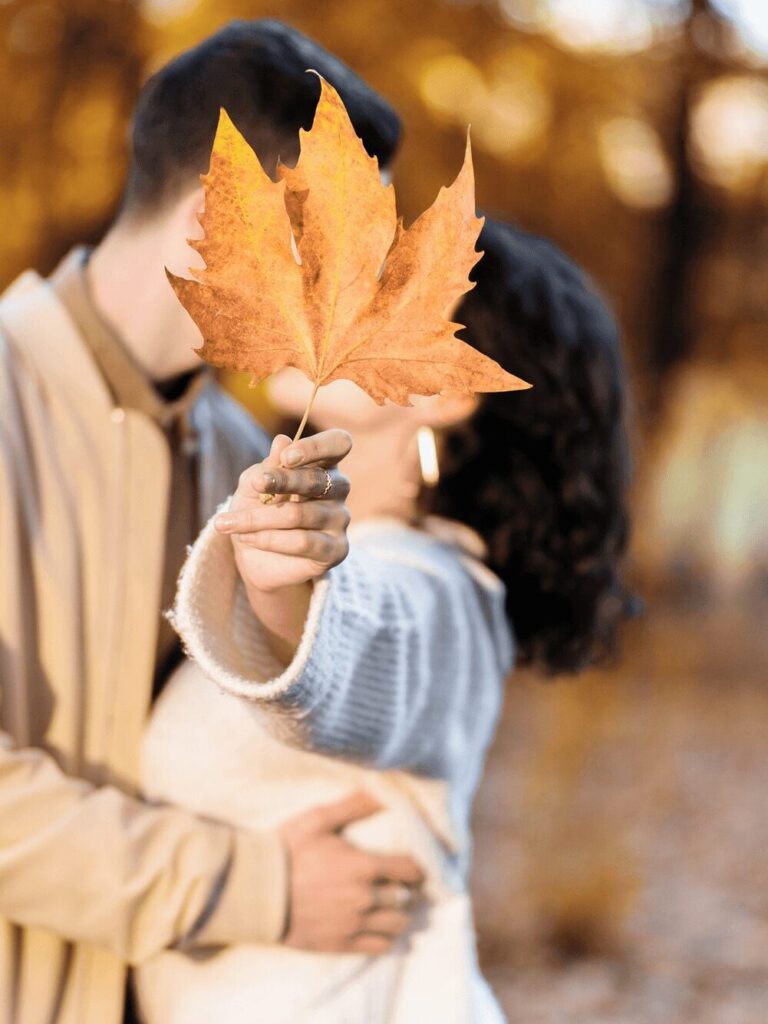Pärchen die sich küssen, aber hinter einem Herbstblatt verstecken.